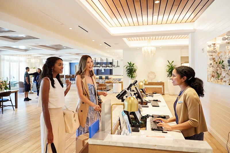 Two guests check in at a bright hotel reception, one staff member assists at the desk with a computer.