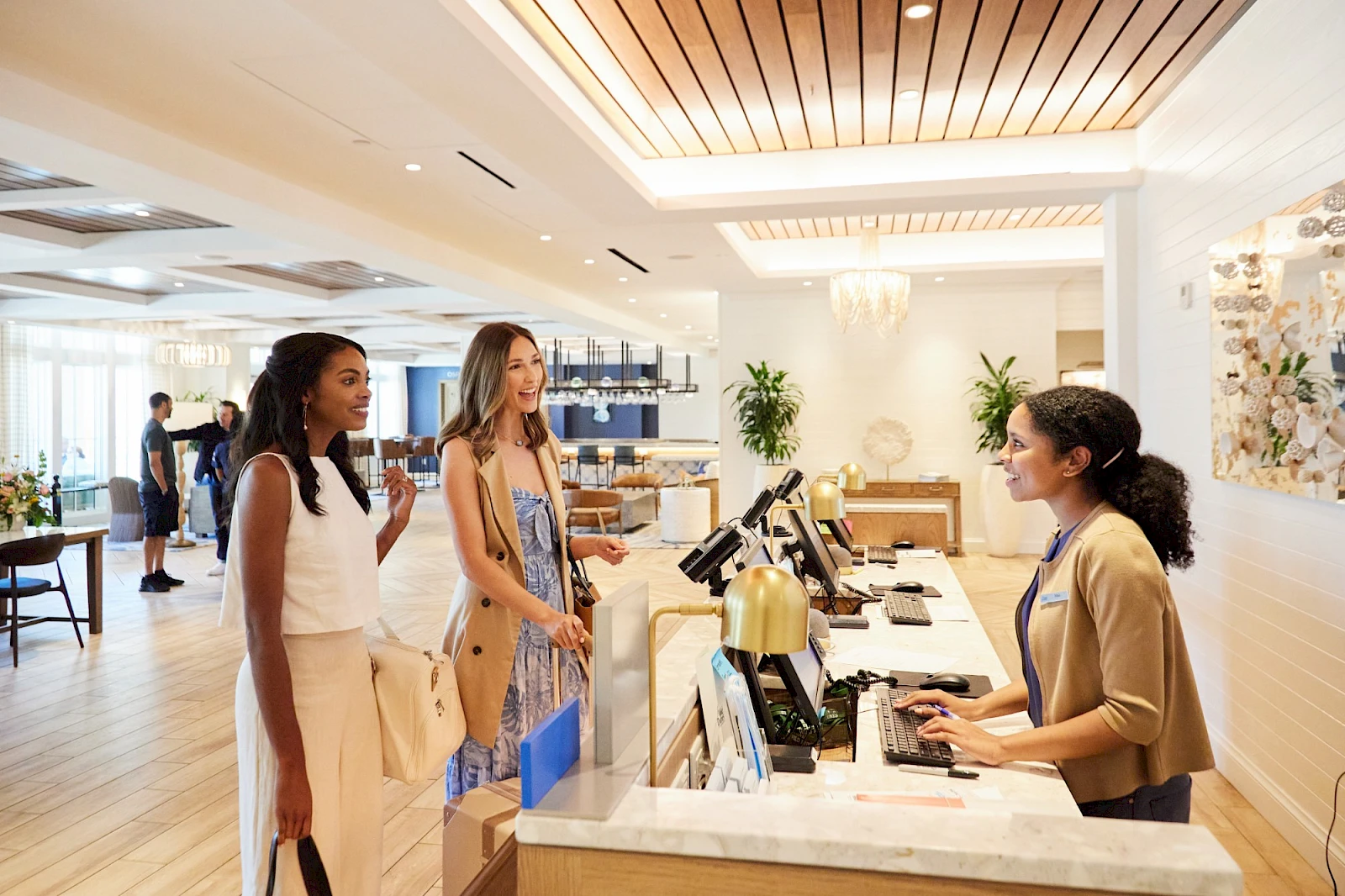 Three women at a hotel check-in desk, with a receptionist helping them in a bright, modern lobby.