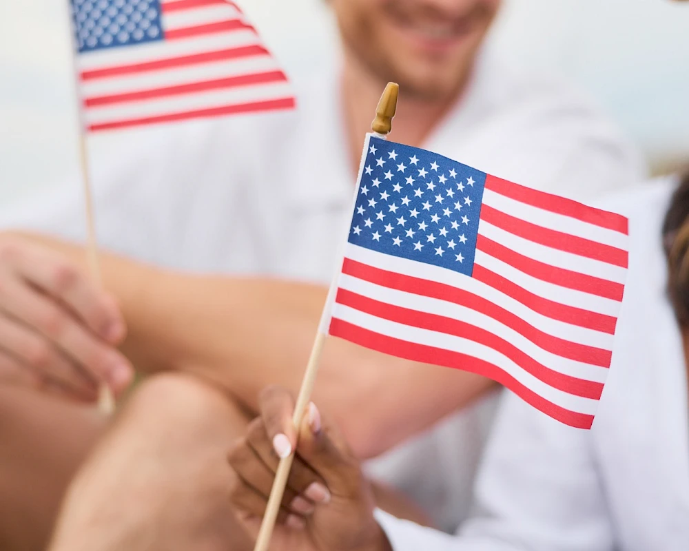 People holding small American flags at a casual outdoor gathering, smiling in the background.