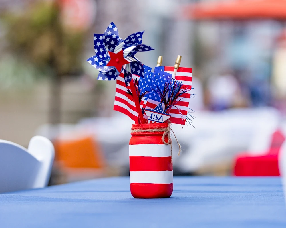 A small bottle centerpiece with striped red and white pattern and patriotic star-spangled pinwheels on a blue tablecloth.