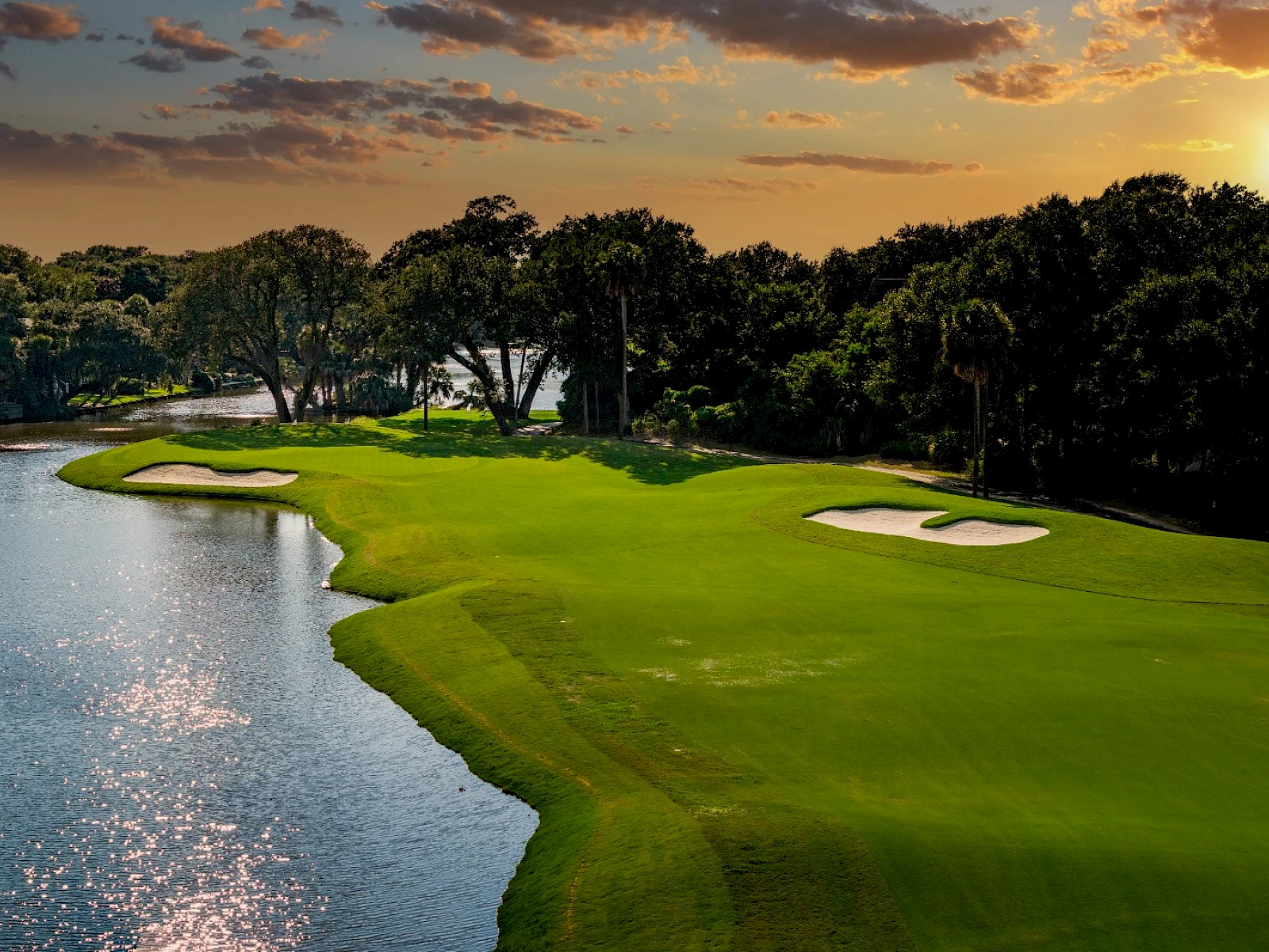 A scenic golf course at sunset, lush green fairways bordered by water hazards and trees, peaceful, inviting players to finish strong.
