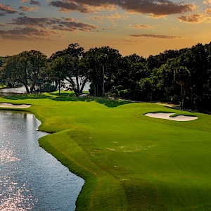 A scenic golf course at sunset, lush green fairways bordered by water hazards and trees, peaceful, inviting players to finish strong.