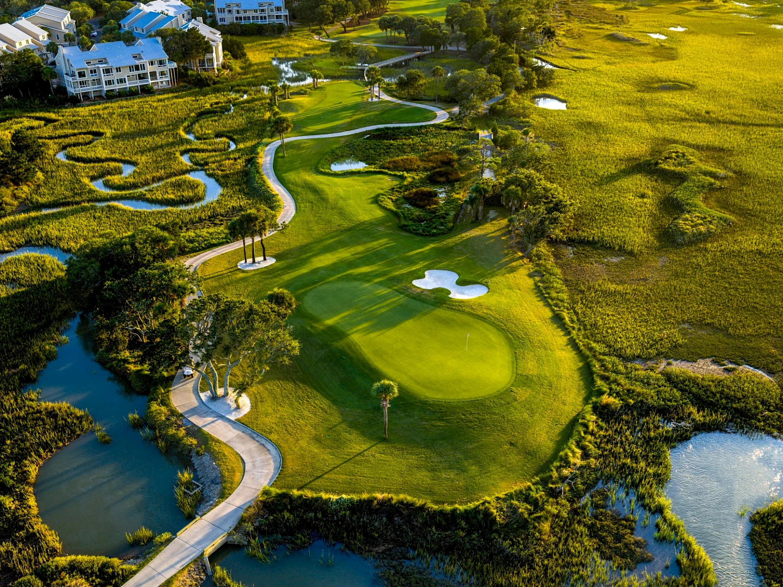 An aerial view of a luxury golf course with greens, fairways, water hazards, winding paths, and surrounding villas in a sunny landscape. End.
