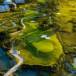 An aerial view of a luxury golf course with greens, fairways, water hazards, winding paths, and surrounding villas in a sunny landscape. End.